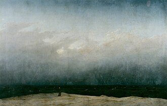 A solitary monk stands on a barren shore facing an immense, dark sea under a vast gray sky. The figure is tiny against the overwhelming expanse of nature.